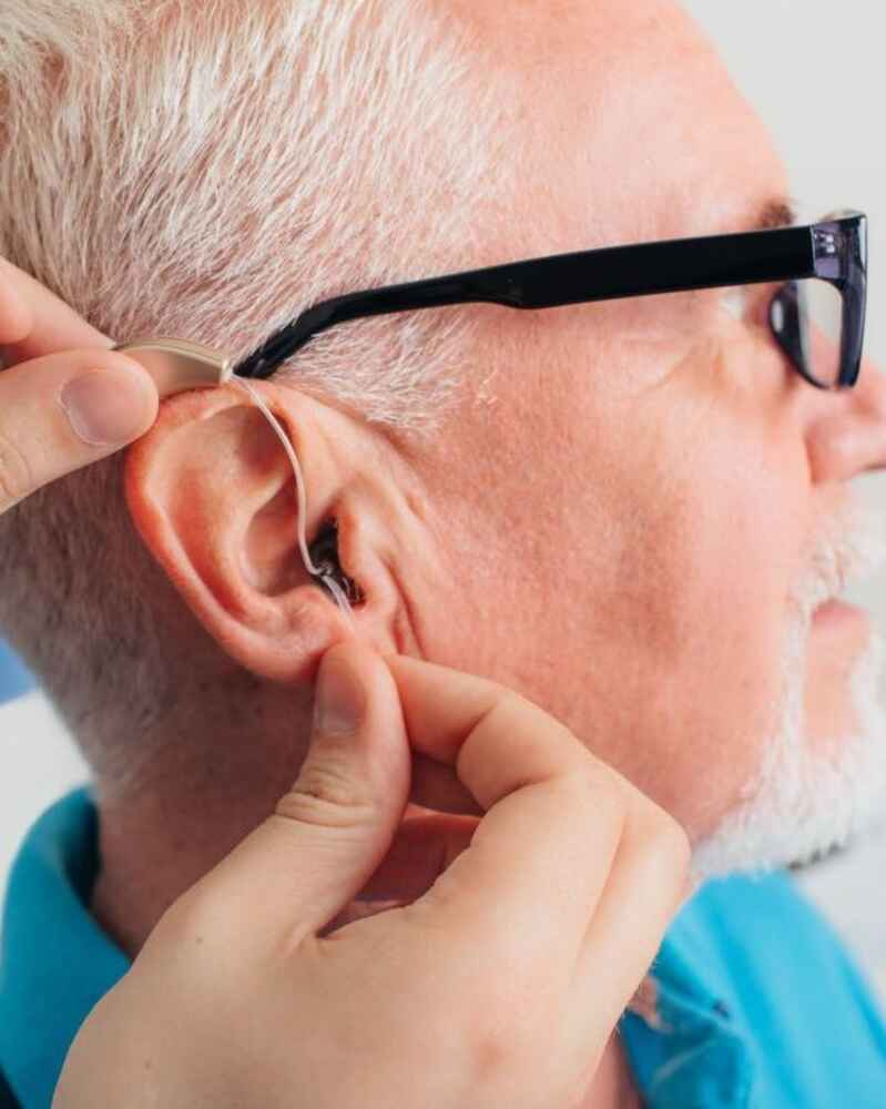 Audiologist adjusting hearing aid on patient