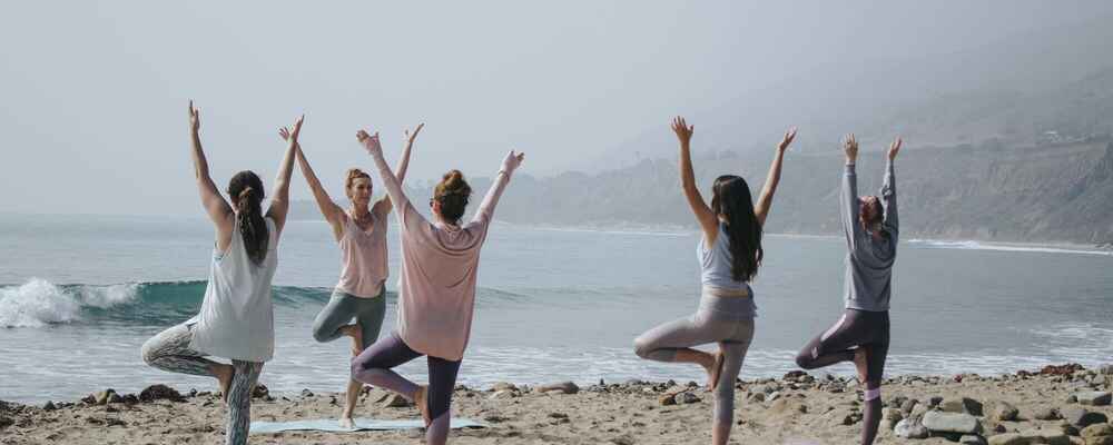 Group of woman practicing balance while doing yoga on a beach